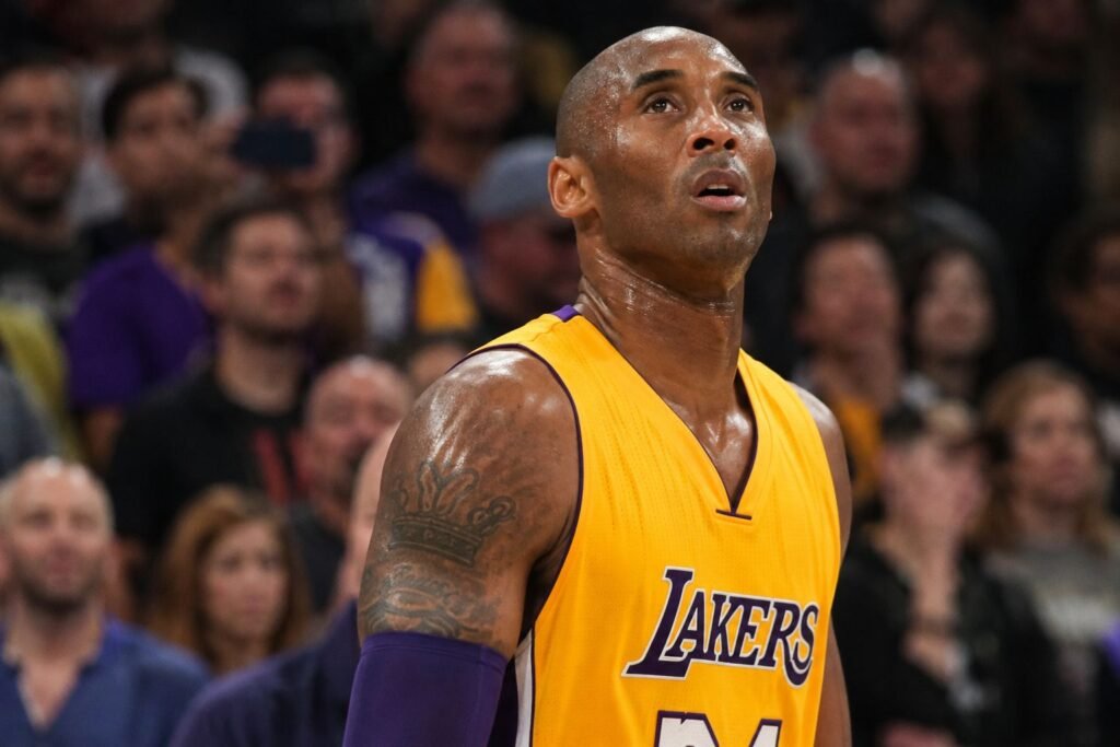 Kobe Bryant in a Los Angeles Lakers jersey looking upward during an NBA game in a packed arena.