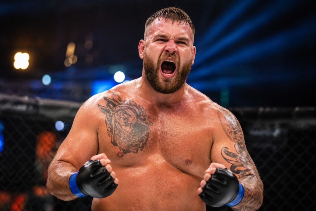 Shane Campbell celebrating inside an MMA cage with clenched fists and a roaring expression